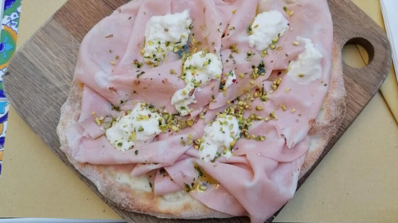 Hotová pinsa s uzeným masem a bílými sýry na dřevěném prknu.