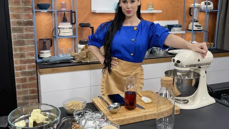 Žena v kuchyni připravuje cukroví s mixérem a surovinami.