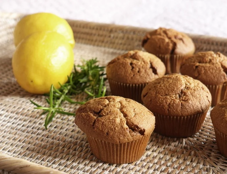 Zlatohnědé citronové muffiny s čerstvými citróny na pleteném podkladu.