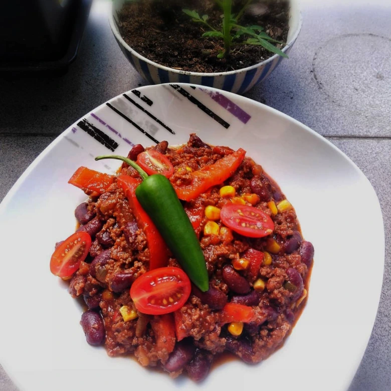 Položka chilli s mletým masem, fazolemi a zeleninou na talíři.