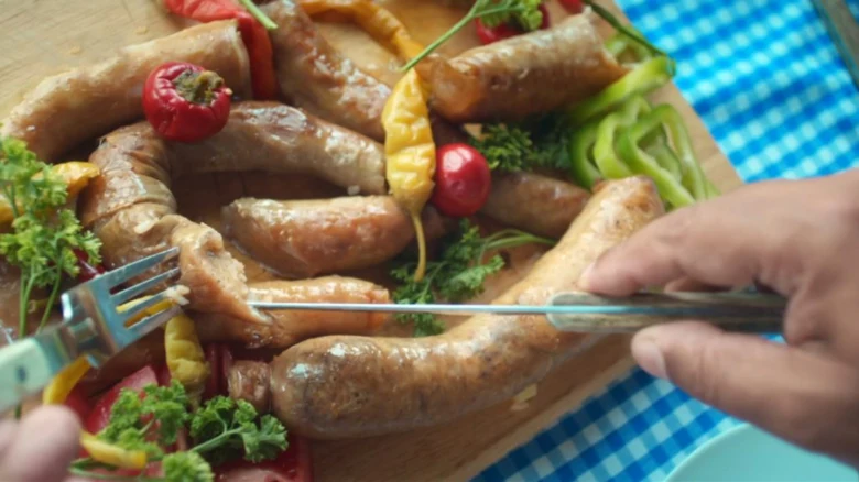 Grilované klobásy s paprikou a petrželkou na dřevěném talíři.