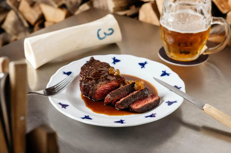 Opečený steak s omáčkou na bílé talíři vedle piva.