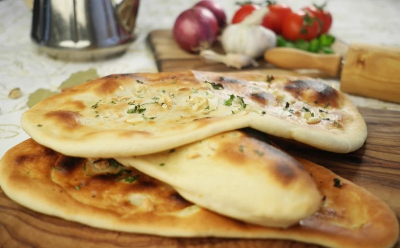 Svěží indické chleby naan s bylinkami na dřevěném talíři.