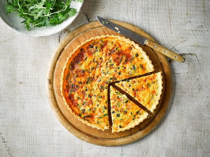 Pečený cibulový quiche s dvěma vybranými kousky na dřevěném podnosu.
