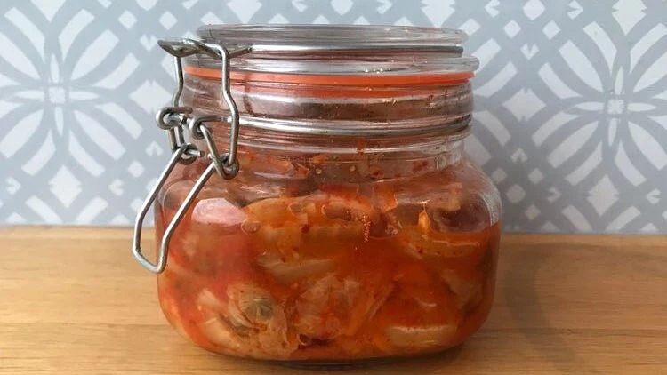 Sklenice s fermentovanou kimchi na dřevěném povrchu.