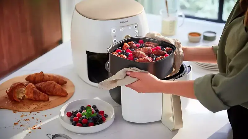 Osoba vyndává pečené ovoce z horkovzdušné fritézy.