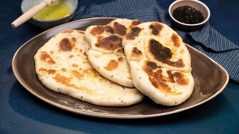 Tři indické placky naan s opečenými skvrnami na talíři.