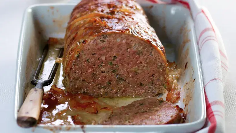 Upečená sekaná nakrájená v keramické mýdlové misce s vidličkou.