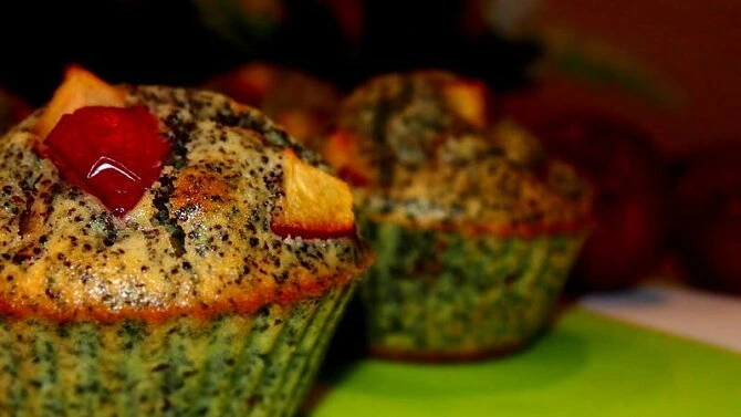 Muffiny s makem a kousky ovoce na zeleném podkladě.
