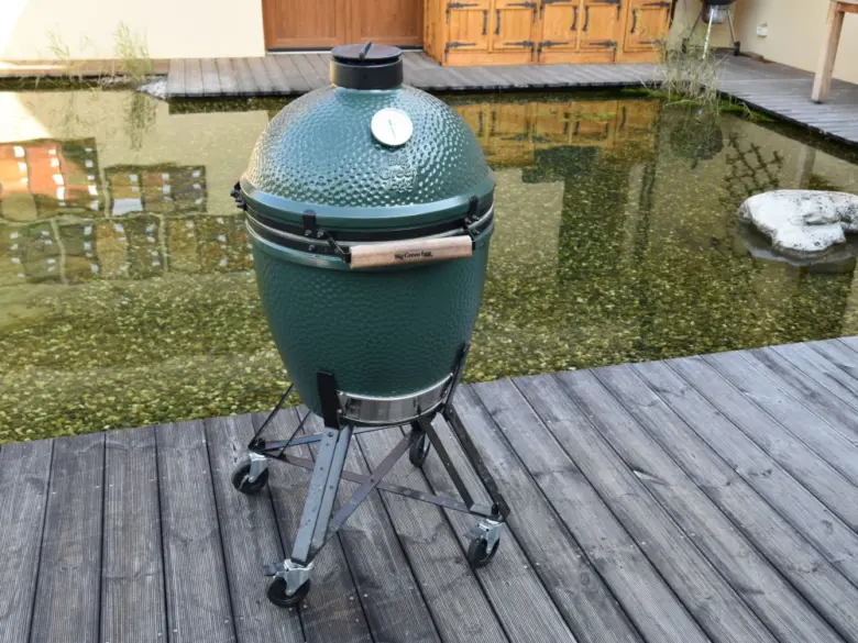 Zelený keramický gril na dřevěné terase u jezera.