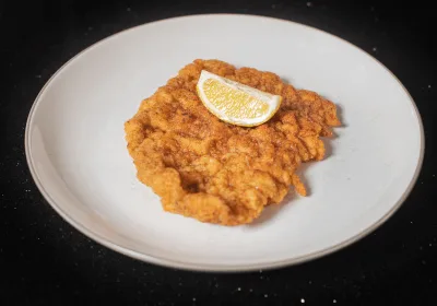 Zlatě opečený telecí řízek s kouskem citronu na bílém talíři.