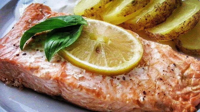 Upečený losos s citronem, bazalkou a bramborami na talíři.