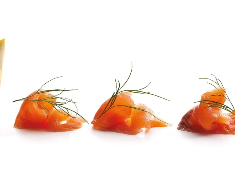 Tři kousky lososa gravlax s koprem na bílém pozadí.