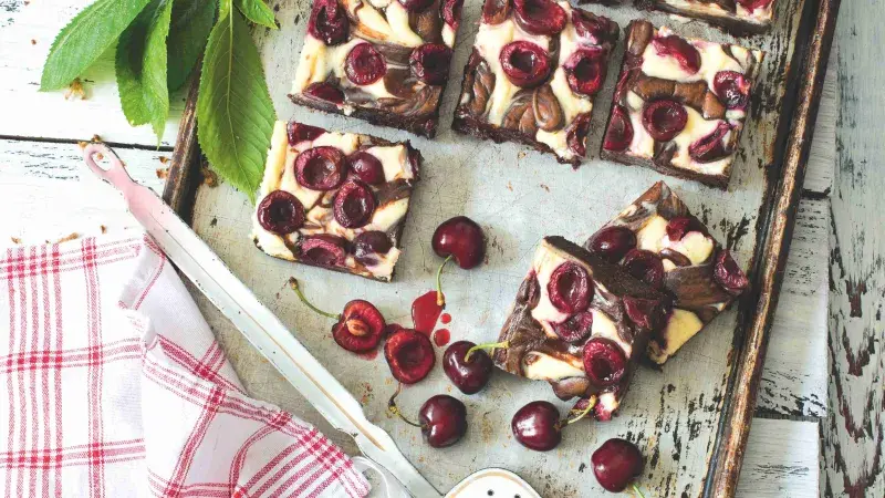Čokoládové brownies s třešněmi na plechu vedle čerstvých třešní.