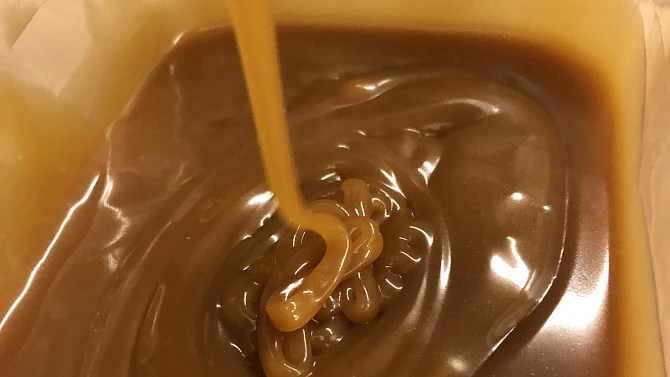 Zlatavý slané karamel se nalévá do nádoby s rozpuštěným cukrem.