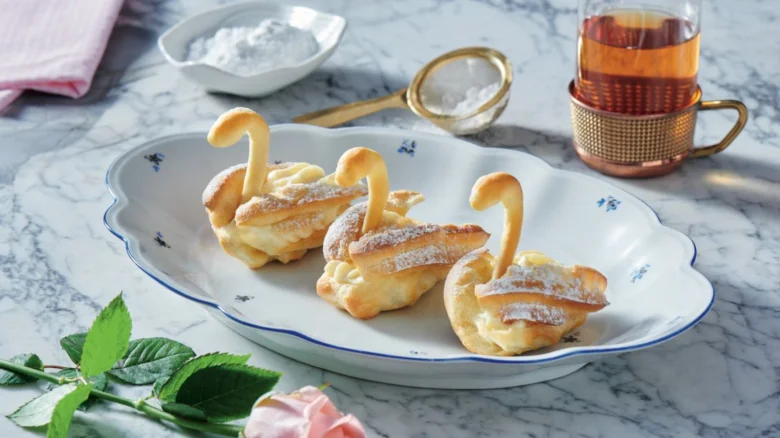 Zlatohnědé svrchní těsto ve tvaru labutí s cukrem na sněhu.
