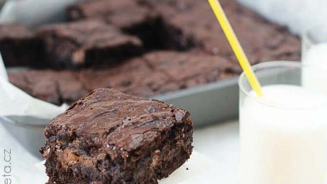 Čokoládový brownie s mlékem v sklenici vedle plechu.
