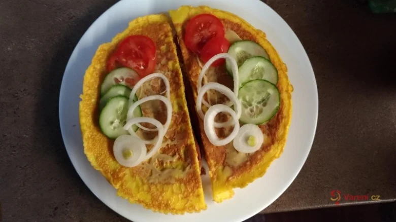 Smaženka s rajčaty, okurkou a cibulí na bílém talíři.