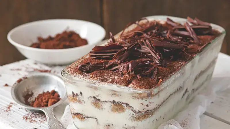 Tiramisu s čokoládovými strouhankami a kakaem v skleněné misce.
