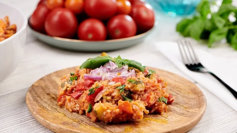 Vegetariánské rizoto s rajčaty, bazalkou na dřevěném talíři.