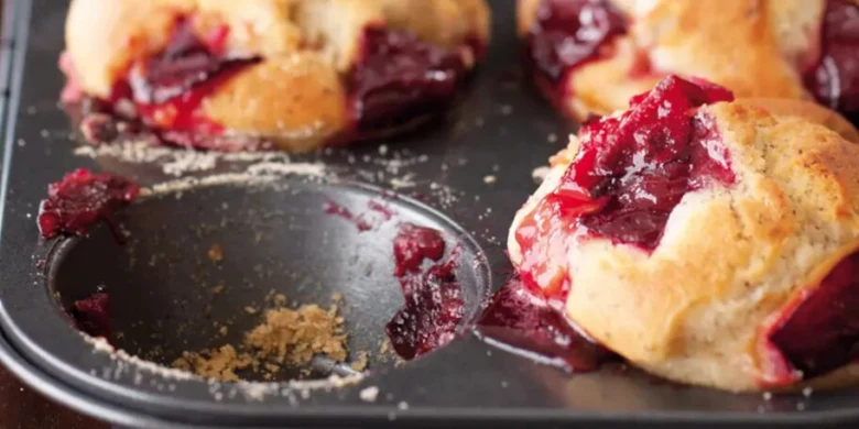 Čerstvé švestkové muffiny v pekáči s viditelným ovocným náplní.