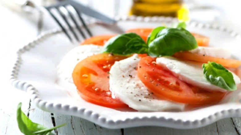 Přesnídaný Caprese s řezy rajčat, mozzarellou a bazalkou.