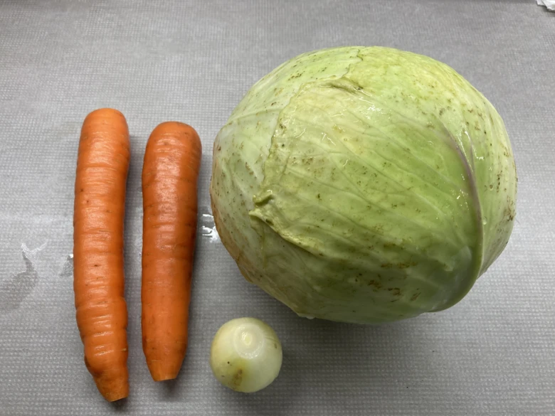 Zelenina pro coleslaw: zelí mrkev a cibule na šedém podkladu.