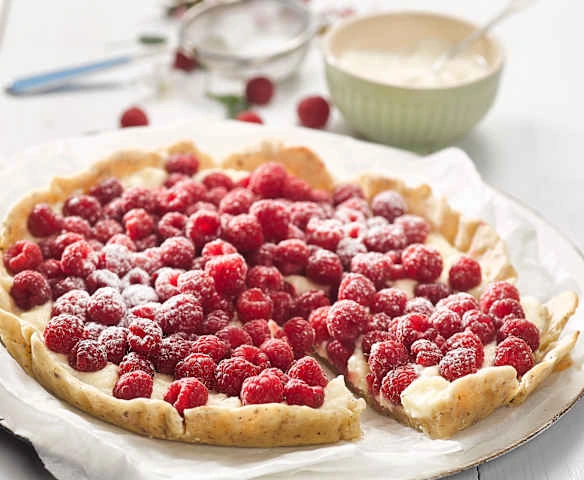 Koláč s malinami a mascarpone posypaný cukrem.