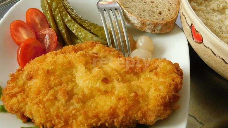 Zlatě strouhaný kotleta s okurkami na bílém talíři.
