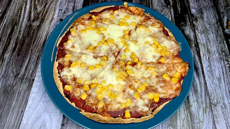 Připravená pizza z tortilly s kukuřicí a sýrem na modrém talíři.