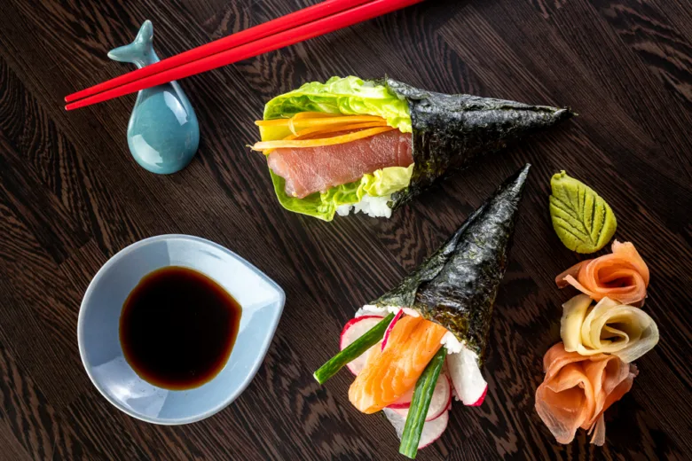 Dva sushi koníky s lososem nebo tuňákem, zeleninou a sójovou omáčkou na tmavém dřevěném stole.