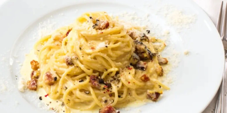 Připravené špagety carbonara s omáčkou na bílém talíři.