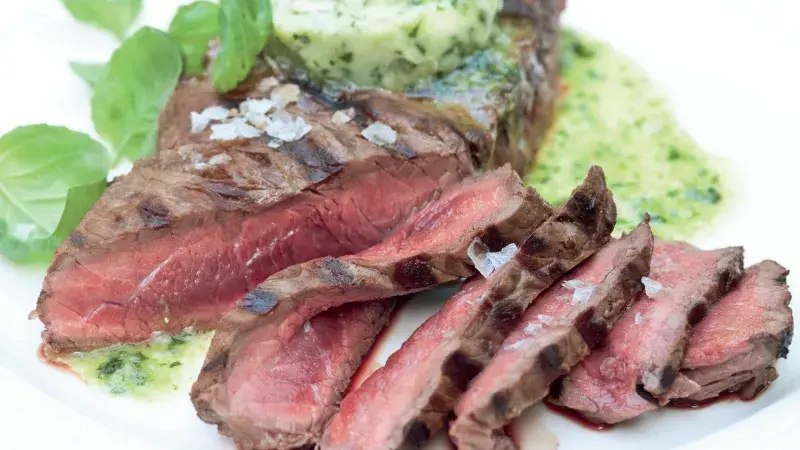 Přezlazený steak s bylinkovou omáčkou na bílé talíři.