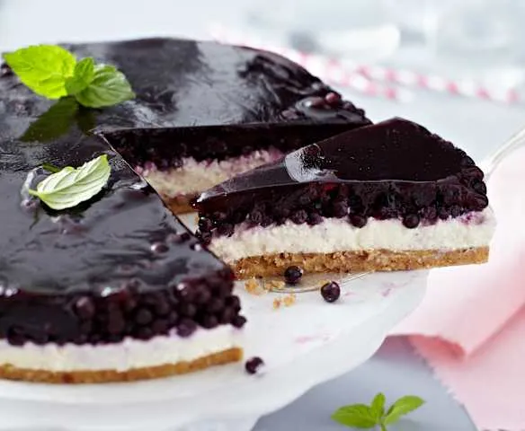 Kousek borůvkového dortu s mascarpone na bílém podstavci.