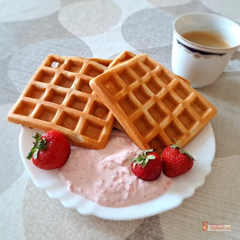Zlaté hrníčkové vafle s jahodovou smetanou na bílém talíři.