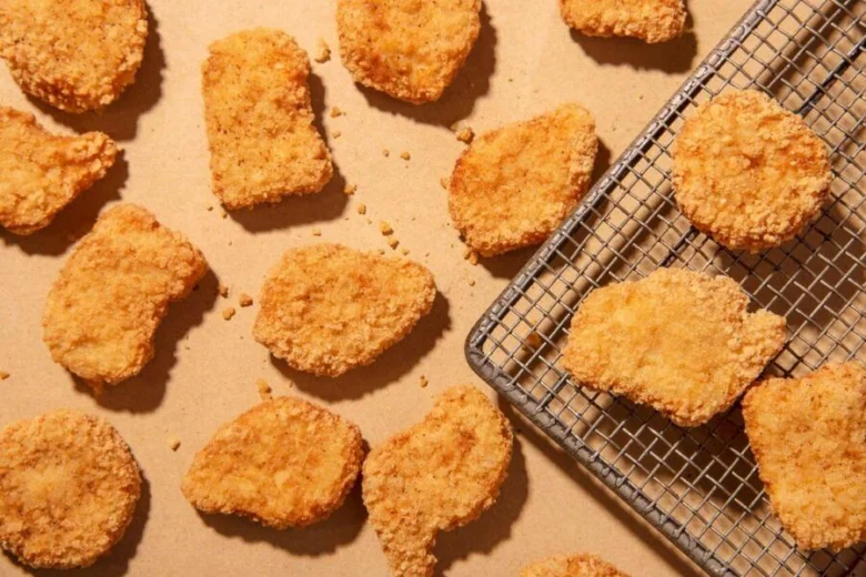Zlatě hnědé kusy panko strouhanky s kuřecími kousky na plechu.