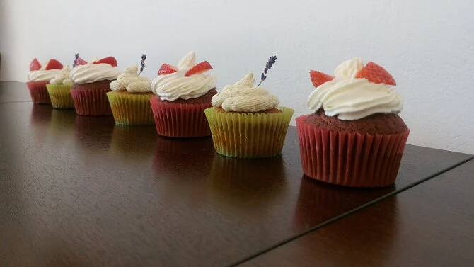 Řada červených muffinů s jahodami a smetanovou šlehačkou.