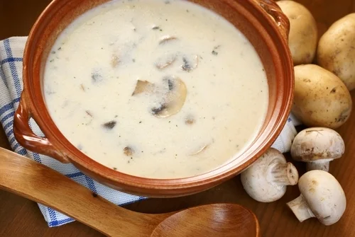 Kremová houbová polévka v hrnci s čerstvými houbami.