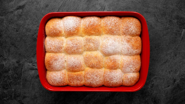Zlatohnědé kynuté buchty v červeném pekáči posypané cukrem.
