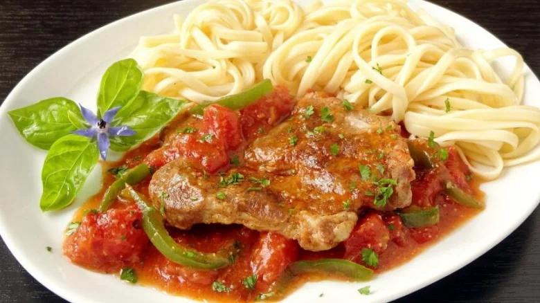 Pork chop s marinádou z rajčat podávaný se špagetami.