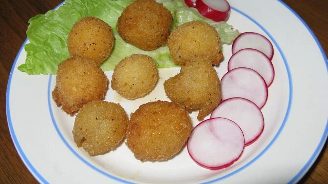 Zlatohnědé bramborové krokety na talíři s okurkou a salátem.