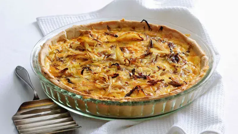 Upečený cibulový quiche v skleněné misce s karameleovanou cibulí.
