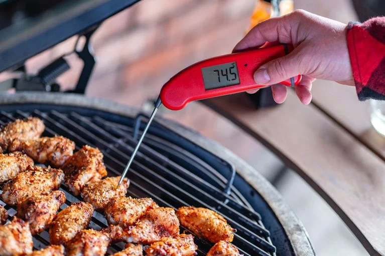 Červený teploměr měří vnitřní teplotu kuřecích křídel na grilu.
