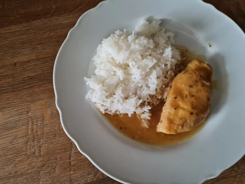 Přírodní kuřecí plátek s rýží v omáčce na bílém talíři.