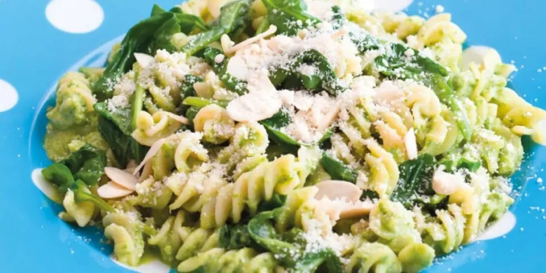 Pasta s špenátovou omáčkou, ořechy a sýr na modré talíři.