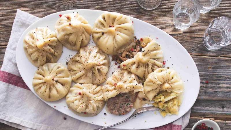 Připravené chinkali s viditelnými náplněmi na bílém talíři.