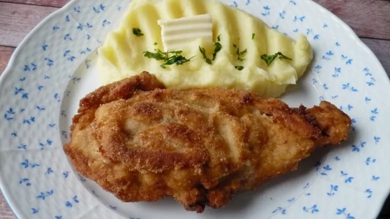 Zlatě opečený řízky s bramborovou kaší na talíři.