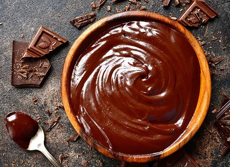 Čokoládová ganache v dřevěné misce s kousky čokolády.