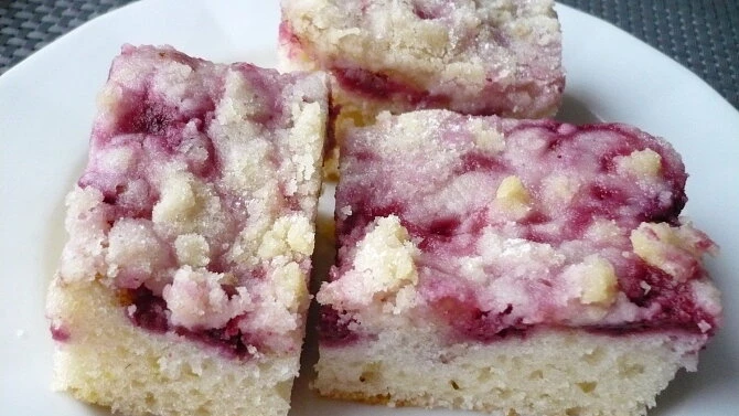 Tři kousky koláče s rybízem a drobenkou na bílém talíři.