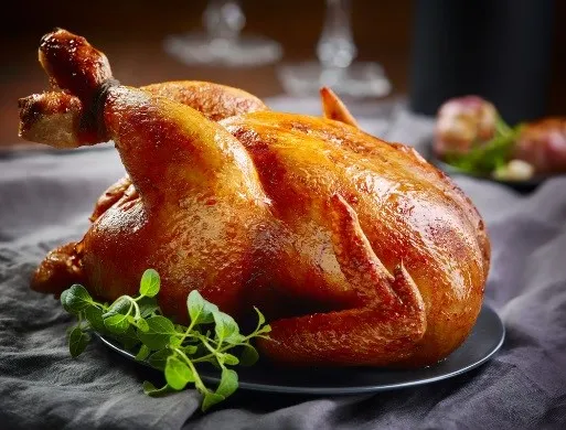 Zlatohnědé pečené kuře na talíři s čerstvou bylinkou.